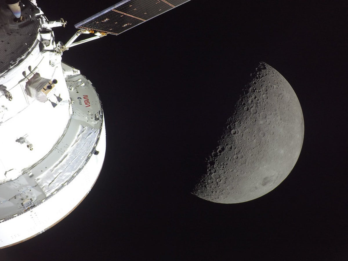 NASA’s Orion spacecraft is seen in the foreground, lit up by the Sun. A first quarter Moon is v...