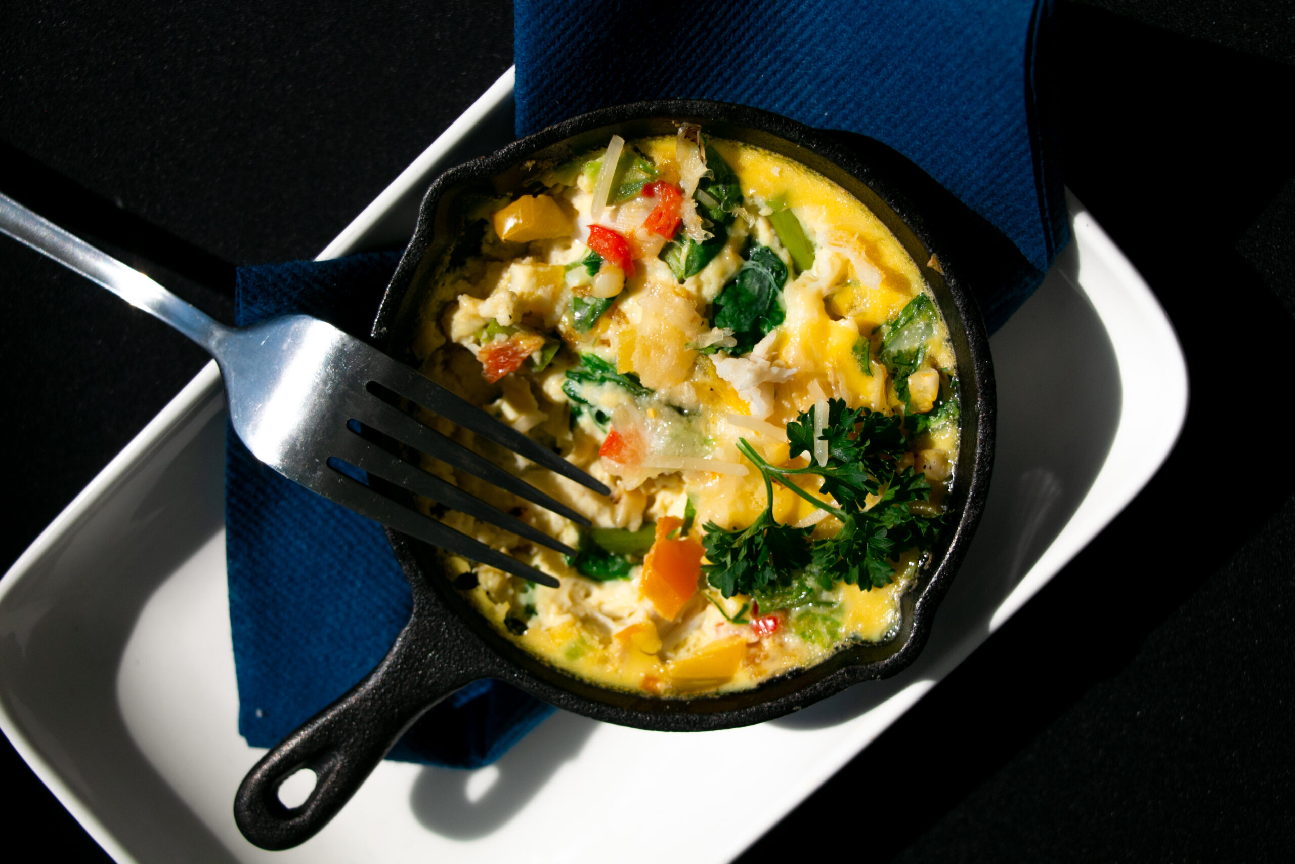 mg-6798 A cooked egg frittata with colorful vegetables sits in a small black cast iron and serving dish a...