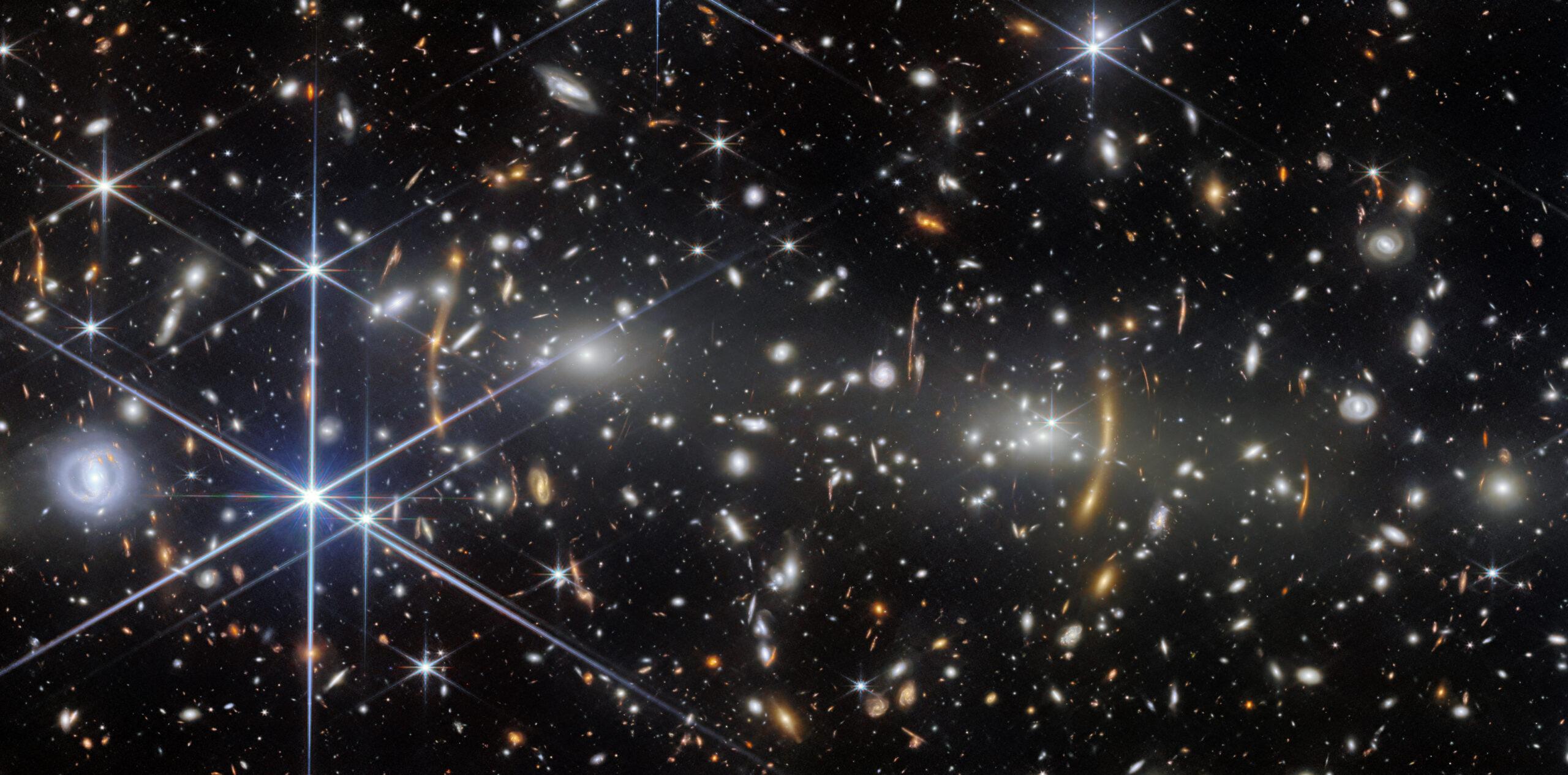 A galaxy cluster in deep space. It is filled with elliptical galaxies: small, bright white glowin...