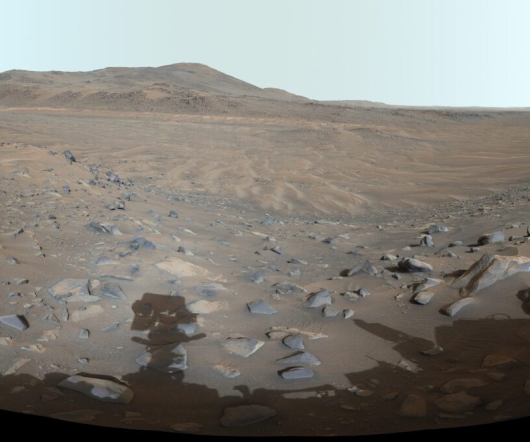 A panoramic view of a barren, rocky landscape with distant hills, framed by parts of a robotic ro...