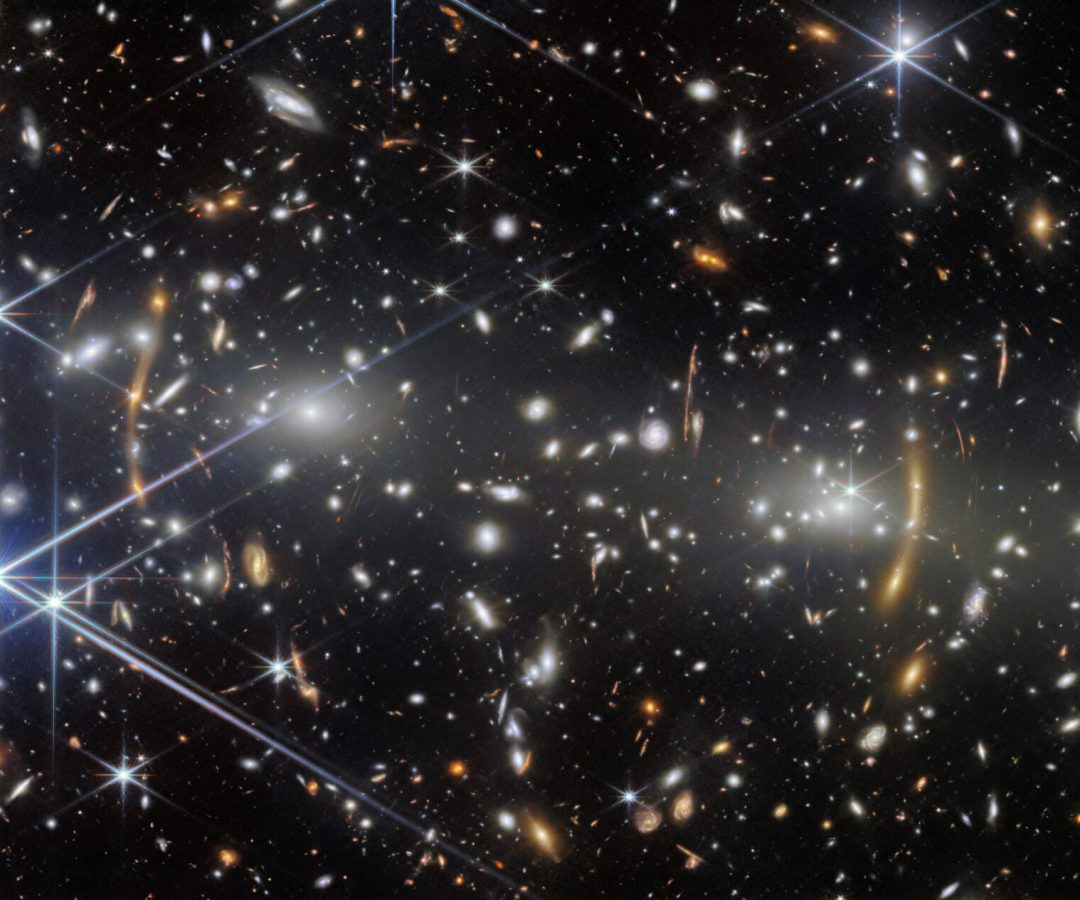 A galaxy cluster in deep space. It is filled with elliptical galaxies: small, bright white glowin...