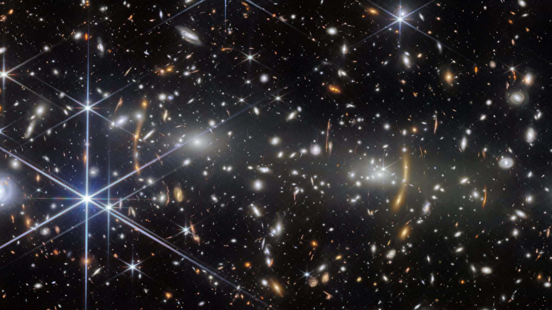 A galaxy cluster in deep space. It is filled with elliptical galaxies: small, bright white glowin...