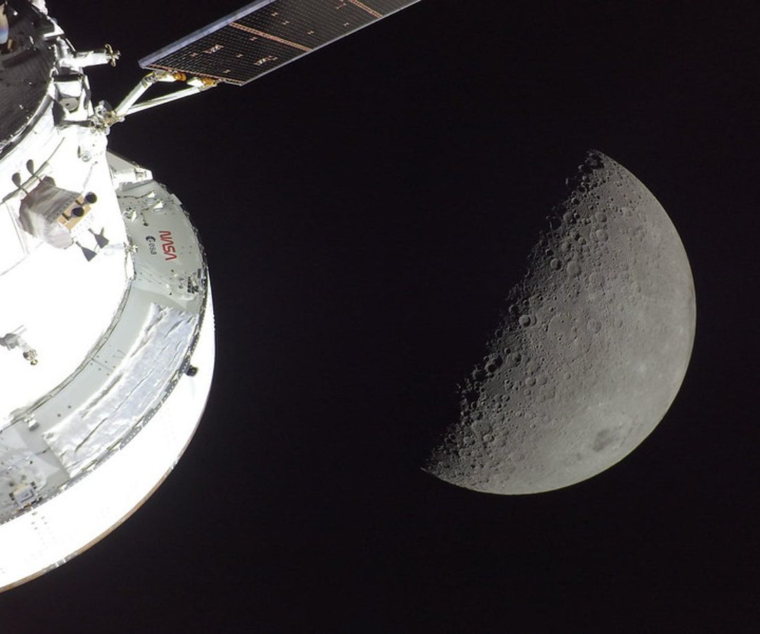NASA’s Orion spacecraft is seen in the foreground, lit up by the Sun. A first quarter Moon is v...