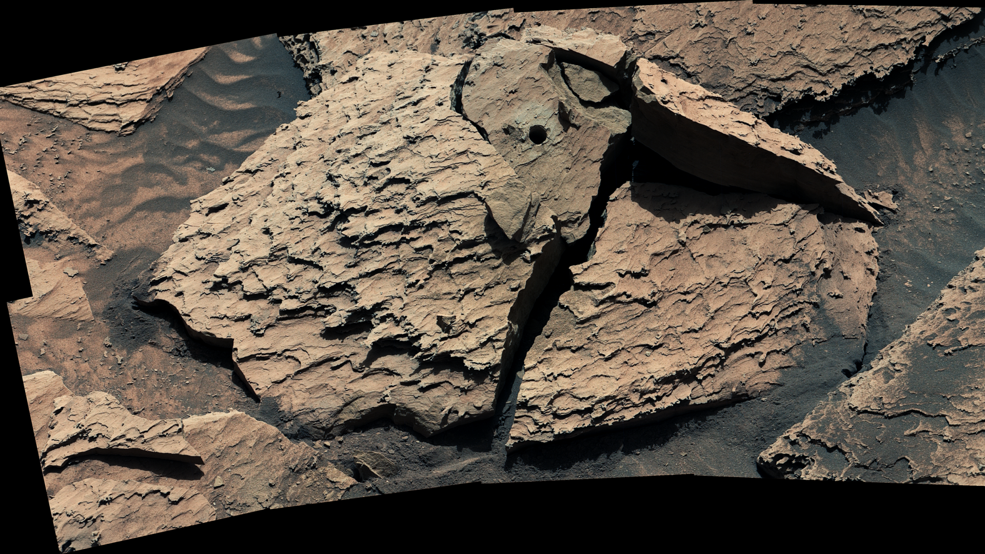 A large, reddish-brown rock as seen by NASA's Curiosity Mars rover. The rock is broken into sever...